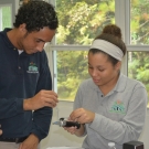 Before students from Forest Heights Academy use equipment in the field, they are practicing using it in the classroom first. Here students are placing a sample of liquid on a refractometer to determine the salinity of the liquid.