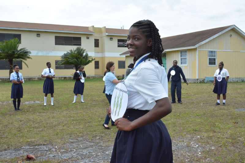 Students at Abaco Central High School participate in a food web activity. Each student is given an animal or plant that can be found in the mangrove food web. A young lady shows that she will be portraying turtle seagrass.