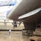 20th January. The water has been emptied and an initial inspection of the hull is being completed. The ship sits on concrete & wooden supports, evenly distributed along the bottom to spread the weight.