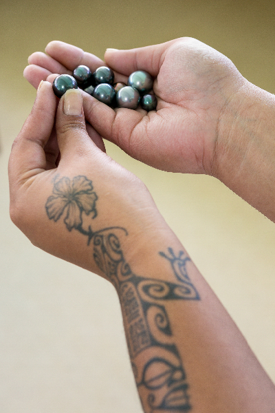 Beautiful black pearls of the Gambier Islands held by a pearl farm technician.  Showing traditional tattooing on arm.
