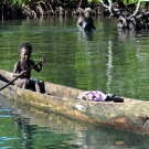 A young child paddles around in his dugout canoe. 