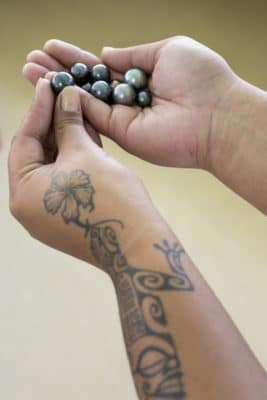 Beautiful black pearls of the Gambier Islands held by a pearl farm technician. Showing traditional tattooing on arm. ©Michele Westmorland/iLCP