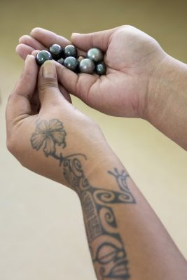 Beautiful black pearls of the Gambier Islands held by a pearl farm technician. Showing traditional tattooing on arm. ©Michele Westmorland/iLCP